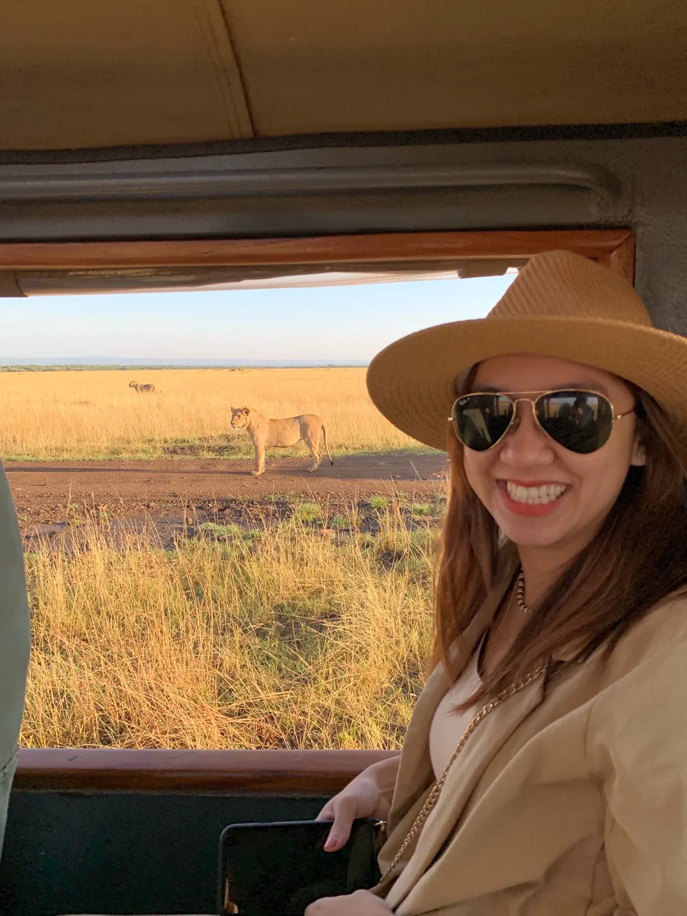 Dee smiling in a safari truck with a lioness behind her