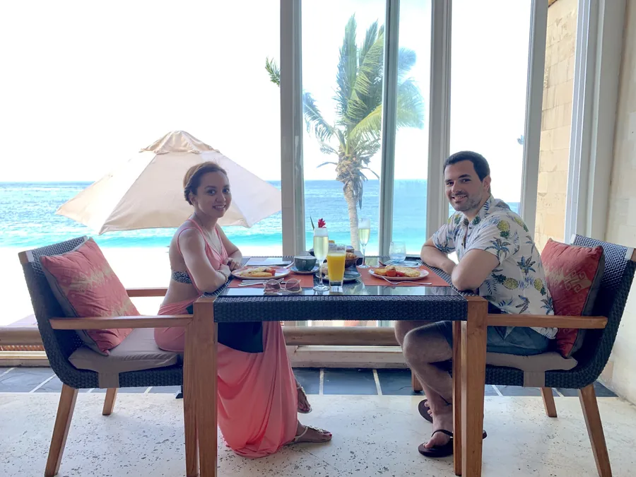 Dee and her husband at breakfast by the window, turquoise sea behind