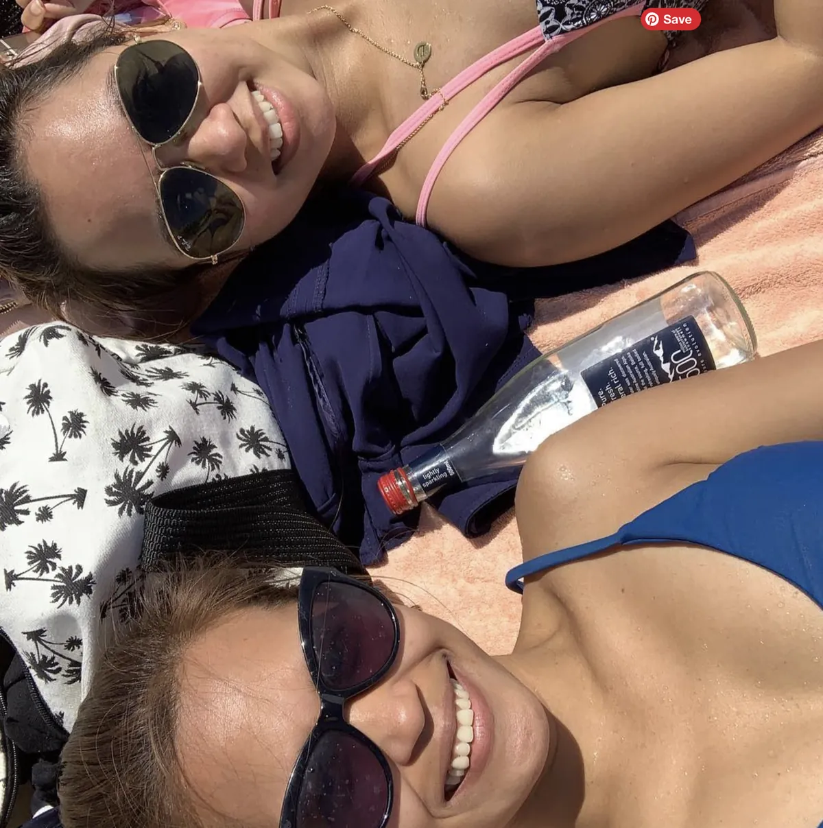Two friends in sunglasses taking a selfie on a beach towel