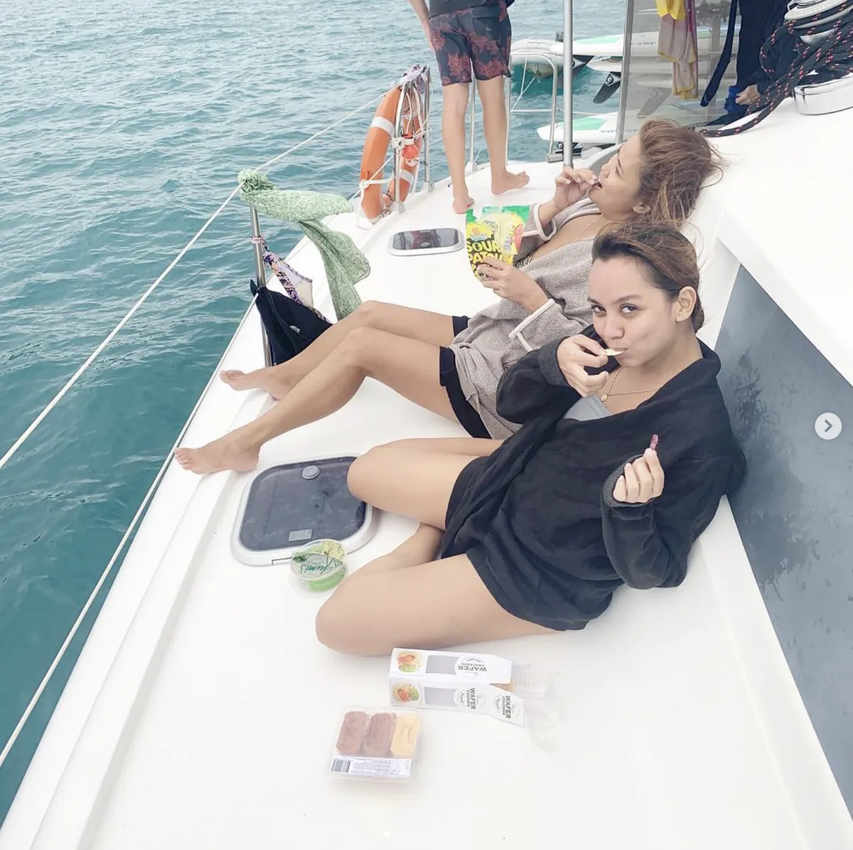 Two friends eating snacks on the deck of a catamaran