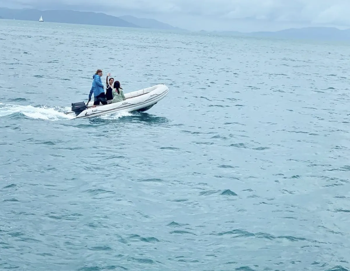 A small inflatable boat with Dee waving, crossing open water