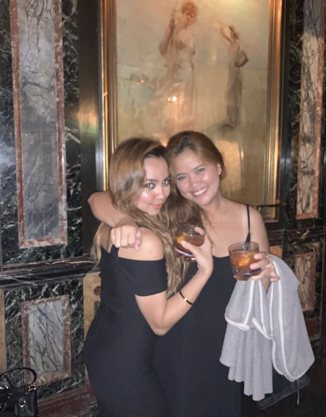 Dee and a friend hugging with drinks in hand
