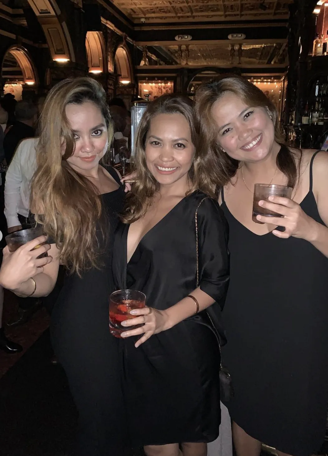 Dee and two friends in black dresses with drinks at a grand Sydney bar