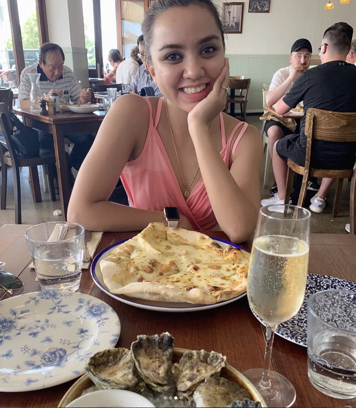 Dee smiling over a pizza, oysters and a glass of sparkling wine