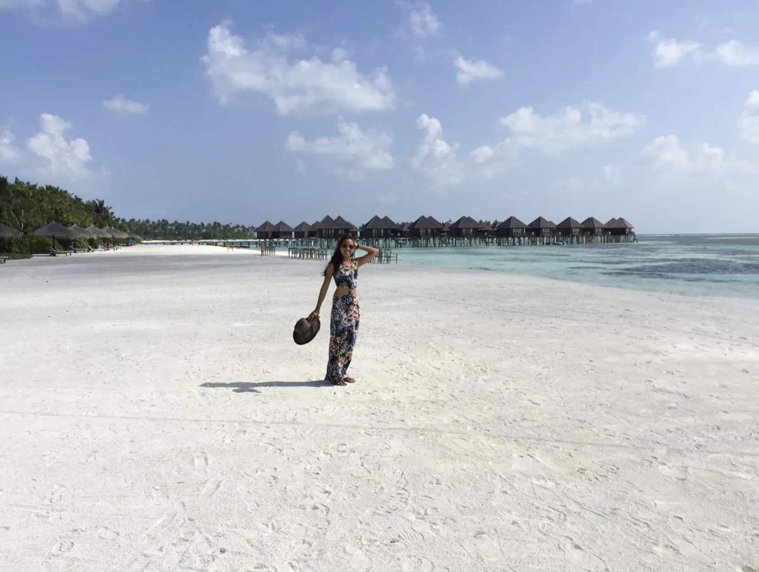 Dee on a white-sand beach in the Maldives, with overwater villas behind her