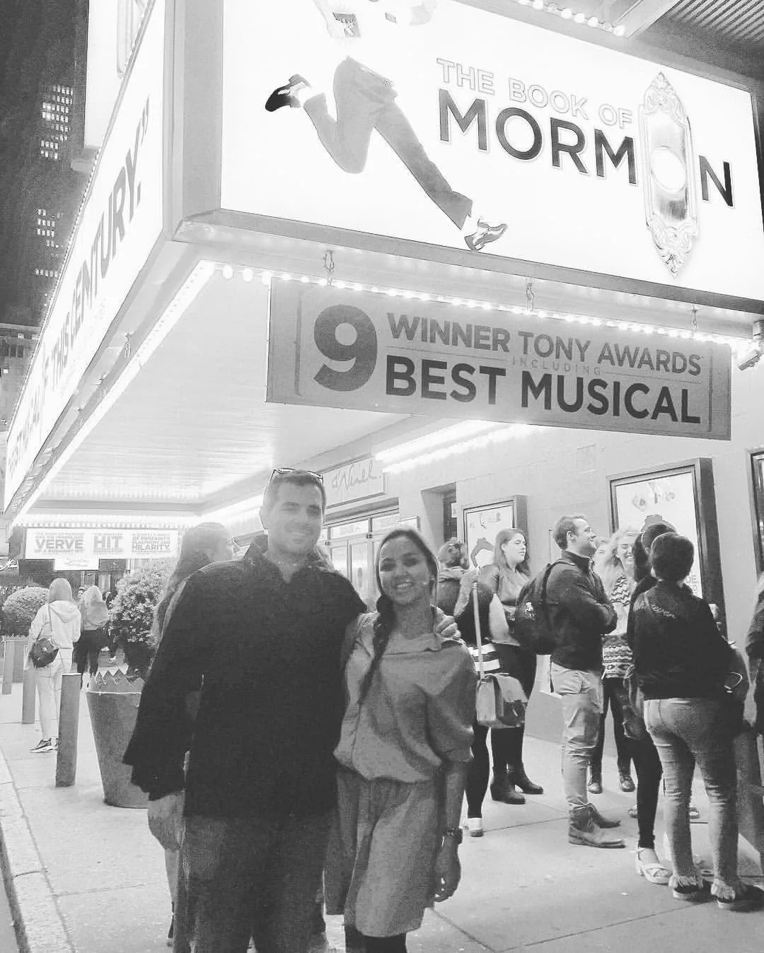 Dee and her husband under The Book of Mormon marquee, in black and white