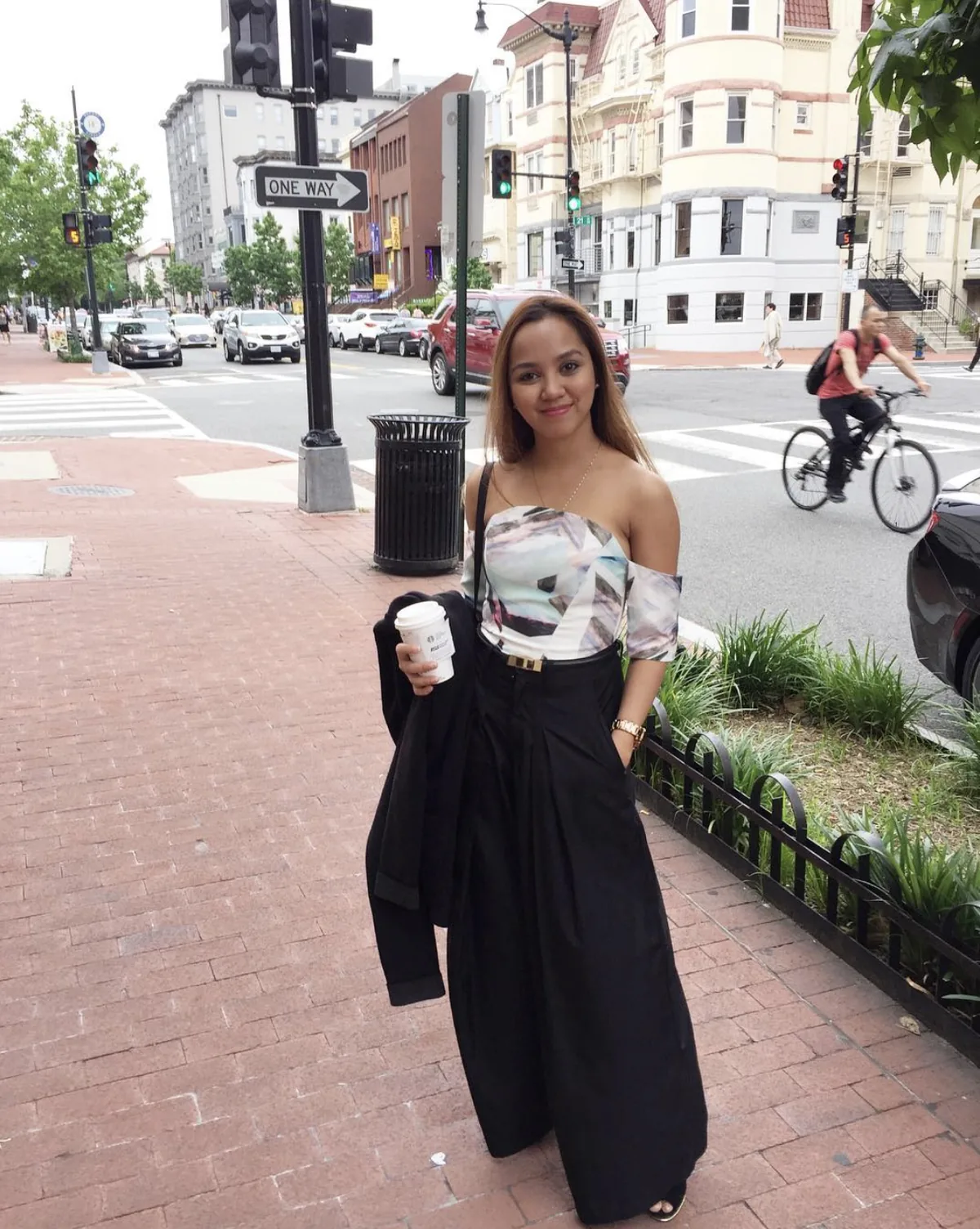 Dee holding a coffee on a red-brick sidewalk at a Washington DC street corner