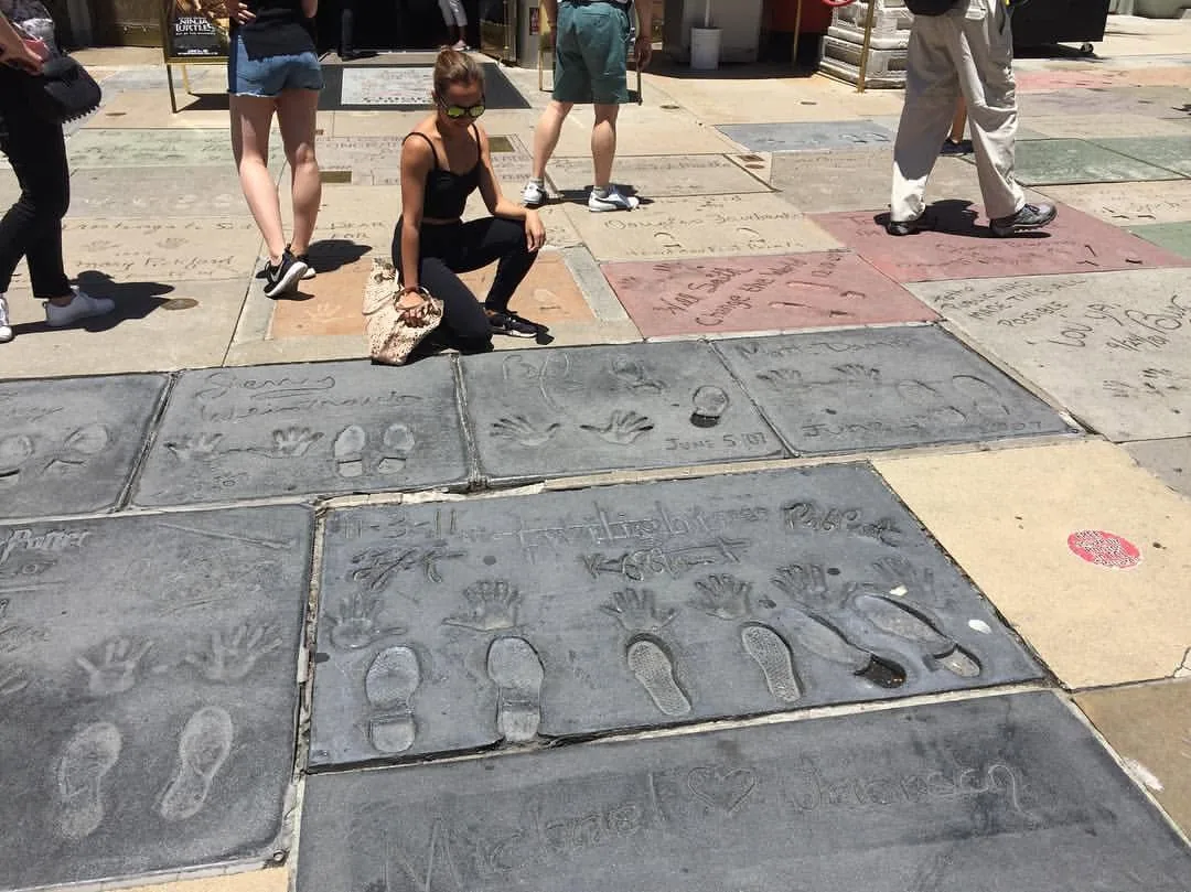 Dee crouching beside celebrity handprints set in concrete