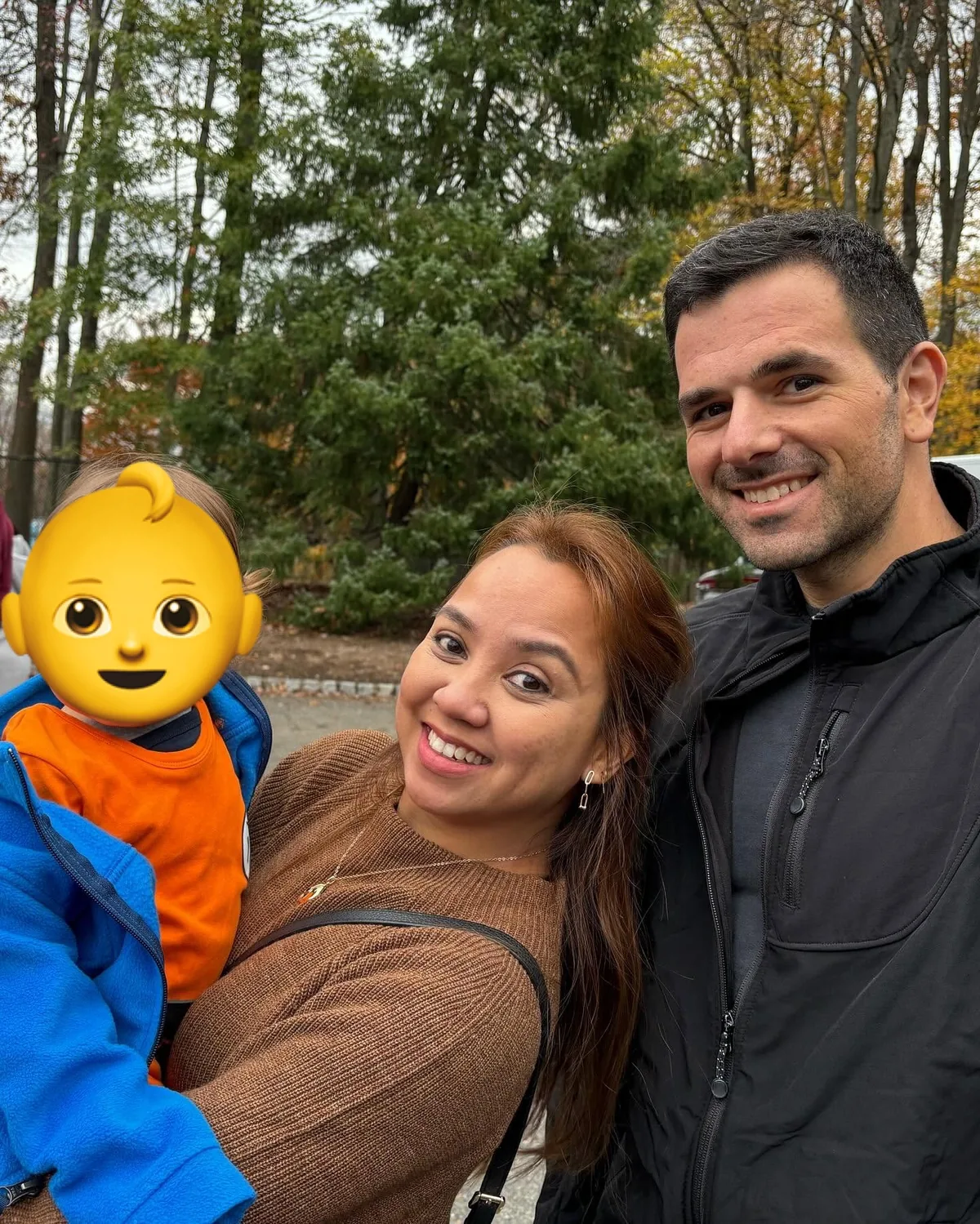 Dee, her husband and their baby smiling under autumn trees