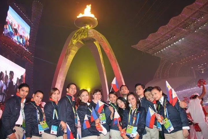 Dee with members of the Philippine team, waving flags beneath a lit cauldron at night